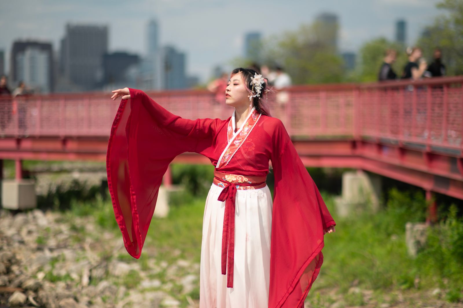 Woman in flowing red Hanfu posing on a bridge against a city skyline