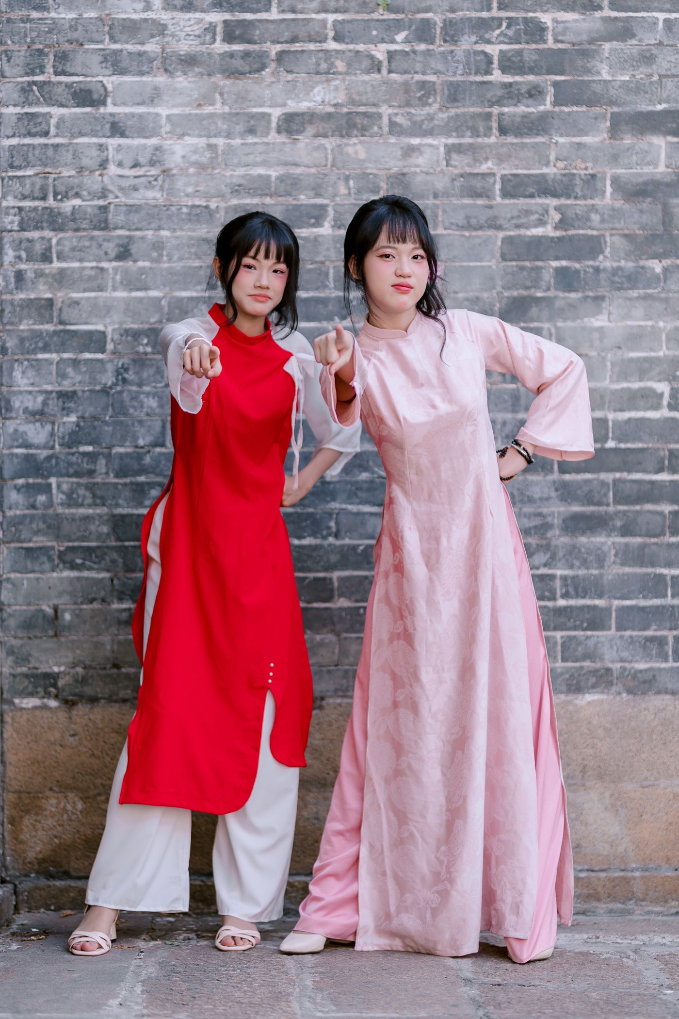 Two young women in traditional Chinese attire posing by a city brick wall
