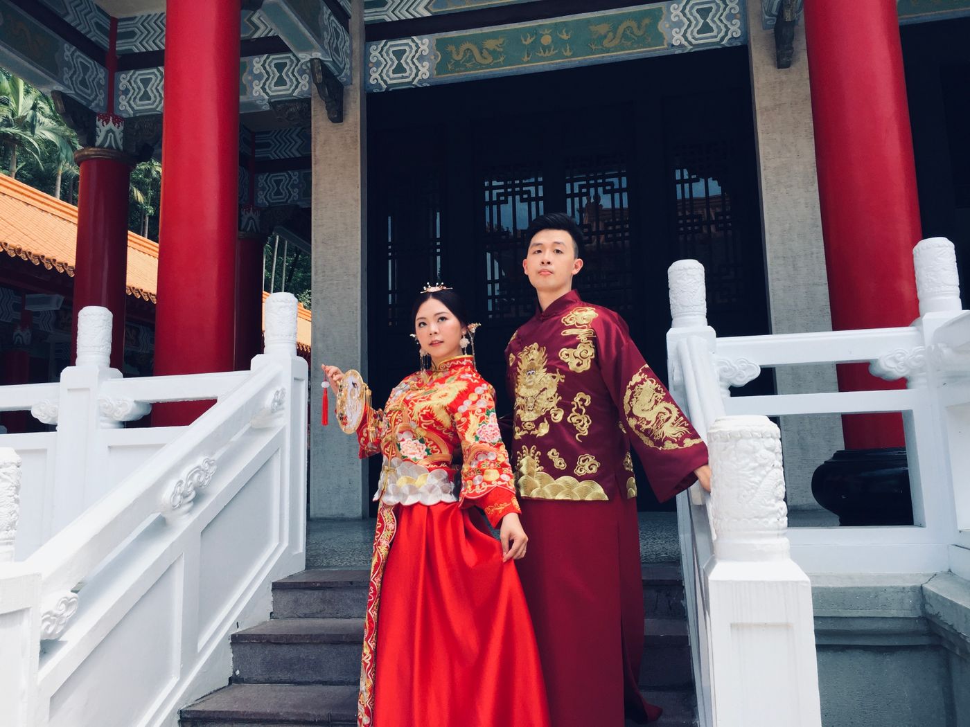 Couple in traditional red Chinese wedding Hanfu outdoors near a temple